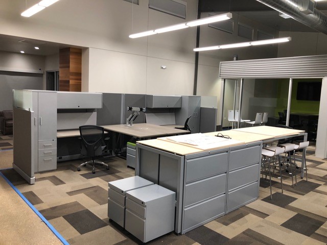 Open office with cubicle workstations, a lateral file island, and a standing-height worktable