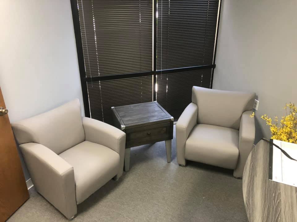 Reception nook with two beige upholstered club chairs and a wood end table